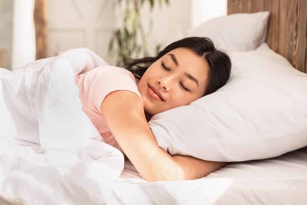Asian Woman Sleeping Lying In Bed At Home Hugging Pillow On Weekend Morning. Healthy Sleep Concept. Problems of Mouth Breathing