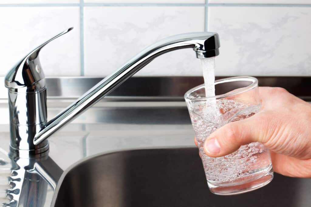 Hand holding a glass of water poured from the kitchen faucet. fluoride question